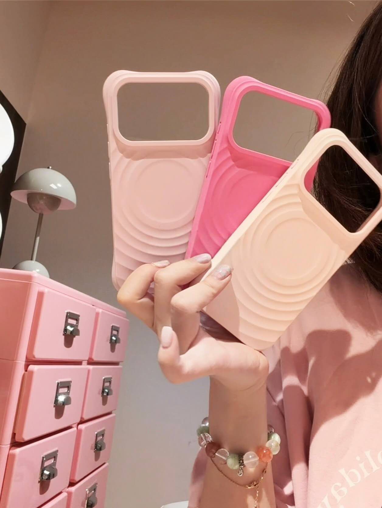 Three pastel ripple-pattern phone cases held in a lifestyle setting